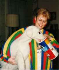 A woman in a colorful striped sweater smiles as she holds a large toy dog, playfully feeding it from a container.