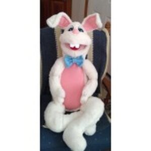 A cheerful, plush bunny with a pink belly and blue bow tie sits on a chair, showcasing a friendly expression. Ideal for festive décor or children's events.