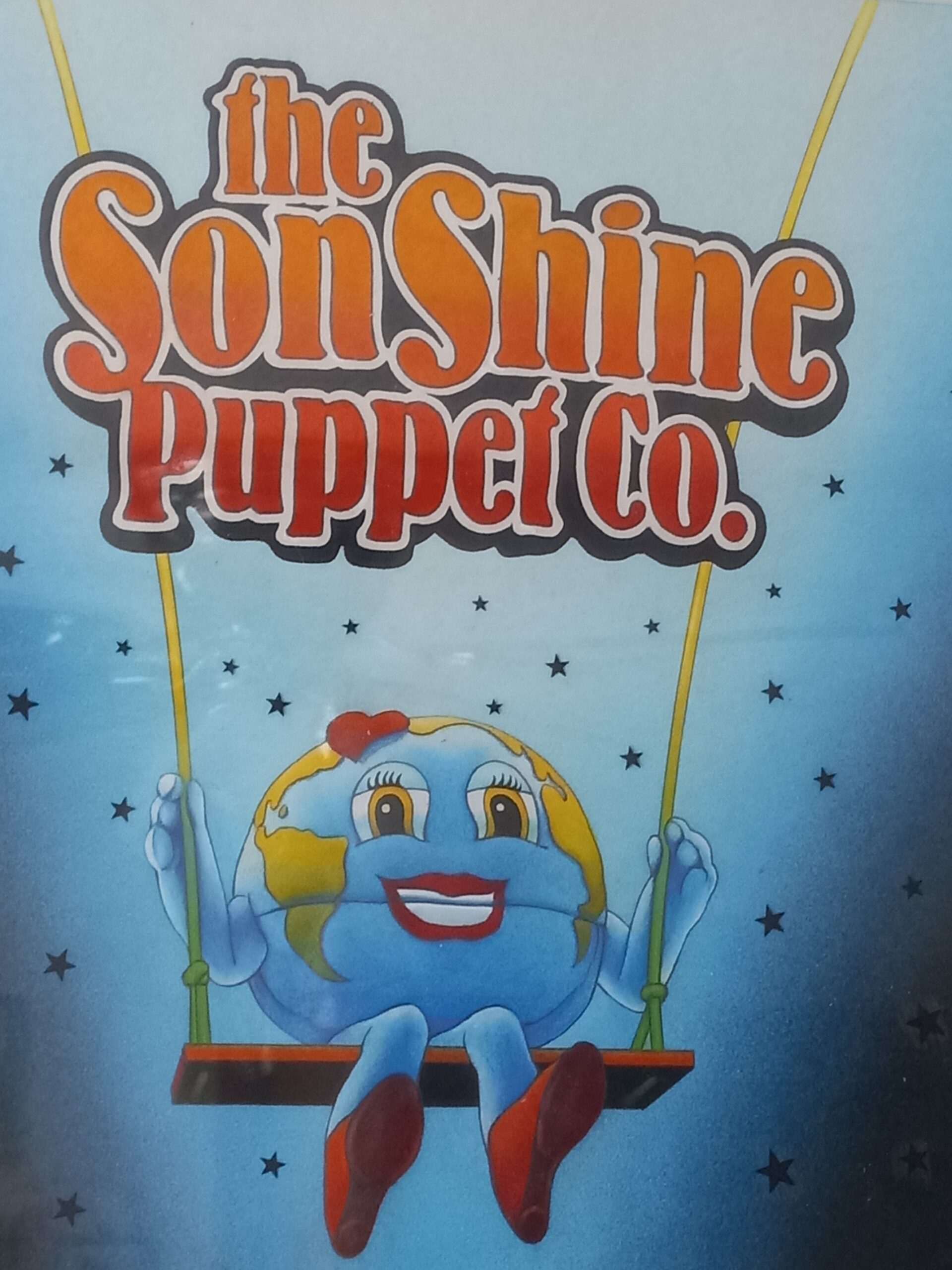 Colorful logo for "The Son Shine Puppet Co." featuring a cheerful, cartoon Earth character on a swing, embodying a playful, whimsical theme.